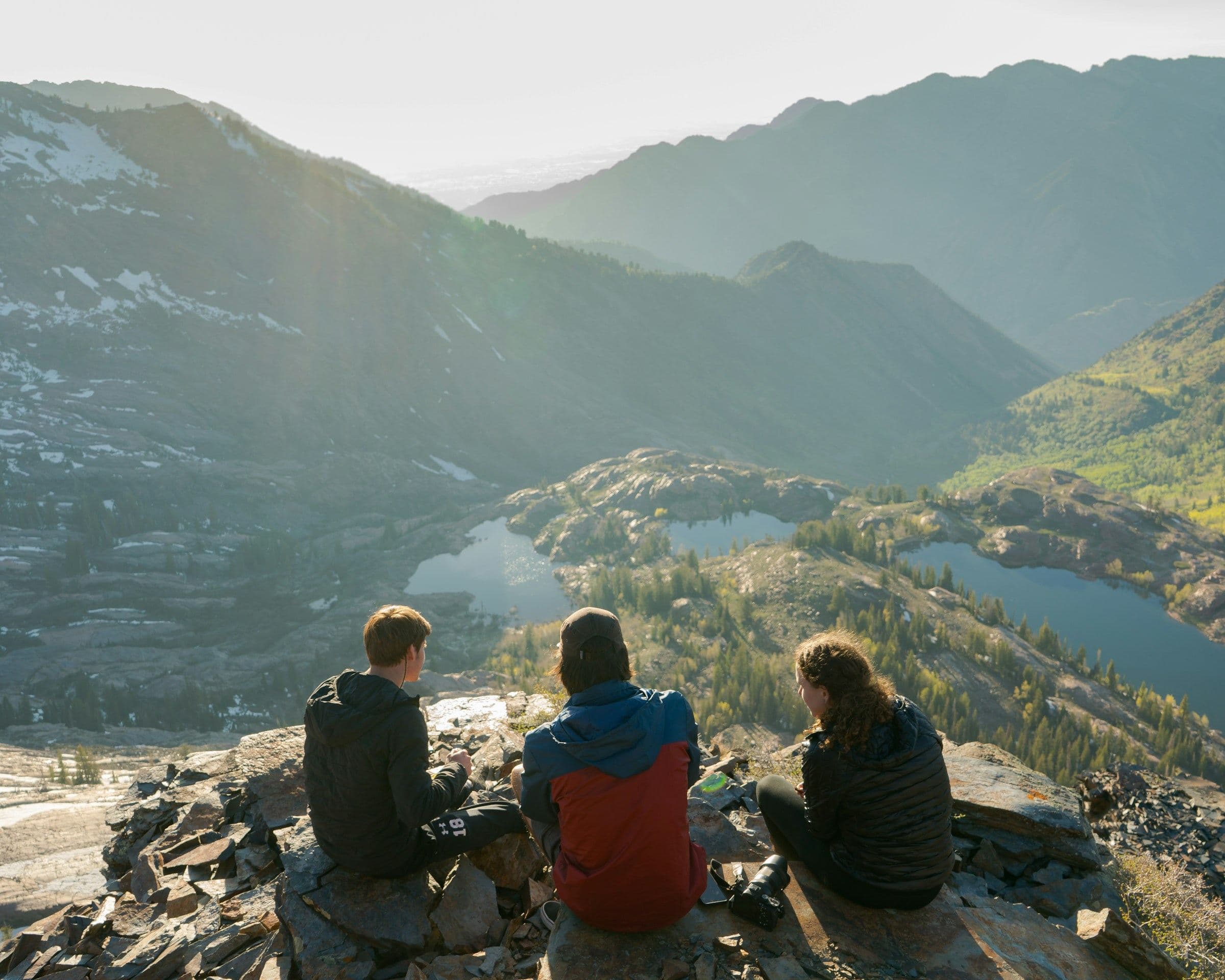 Trois randonneurs assis au-dessus d'un lac entouré de montagnes.